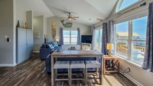 A spacious living area with a wooden dining table, blue sofa, and a large window with a view of the beach. - Beachside Serenity Awaits at 'Knot A Worry'" (Surf City)