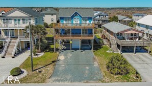 A coastal residential area with multiple houses, including a prominent two-story house with a balcony and a covered porch. - Beachside Serenity Awaits at 'Knot A Worry'" (Surf City)