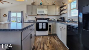 A modern kitchen with grey cabinets, a microwave, a stove, and a refrigerator. - Beachside Serenity Awaits at 'Knot A Worry'" (Surf City)