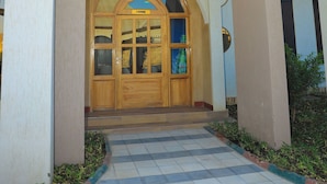 A building entrance with a wooden door and a tiled pathway leading to it. - Rostel Villa Hotel (Mbeya)