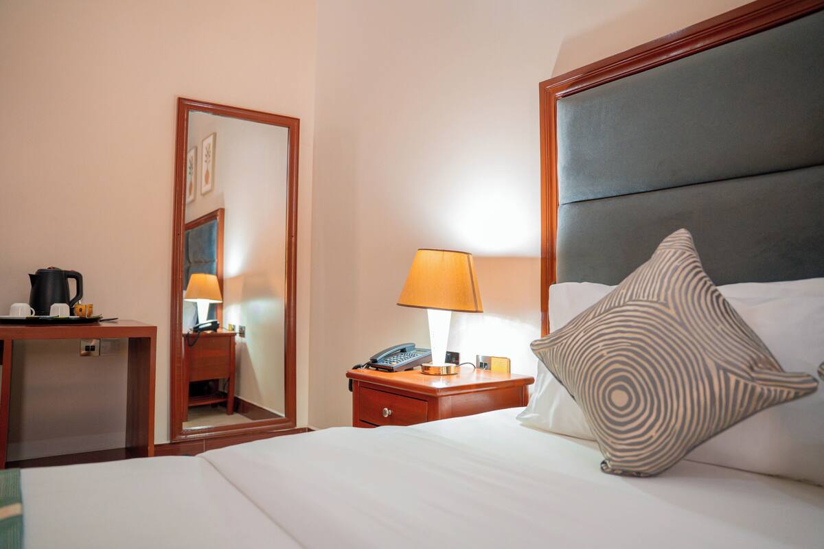 A hotel room with a bed, a bedside table with a lamp, a telephone, and a coffee maker.