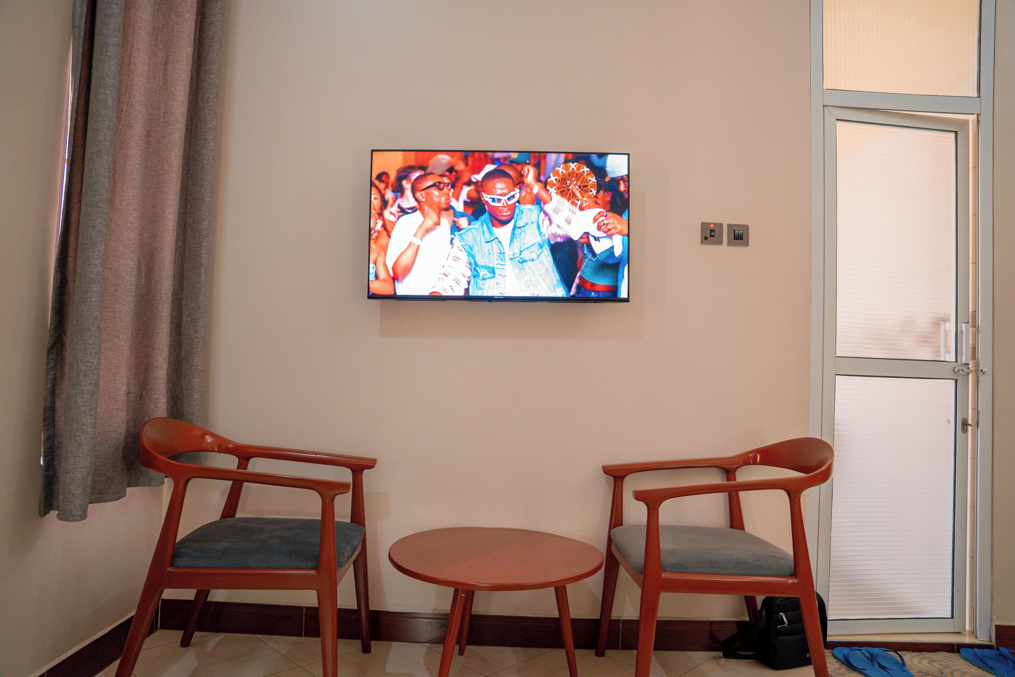 Una stanza con due sedie, un tavolino, una televisione fissata al muro e una porta con un vetro.