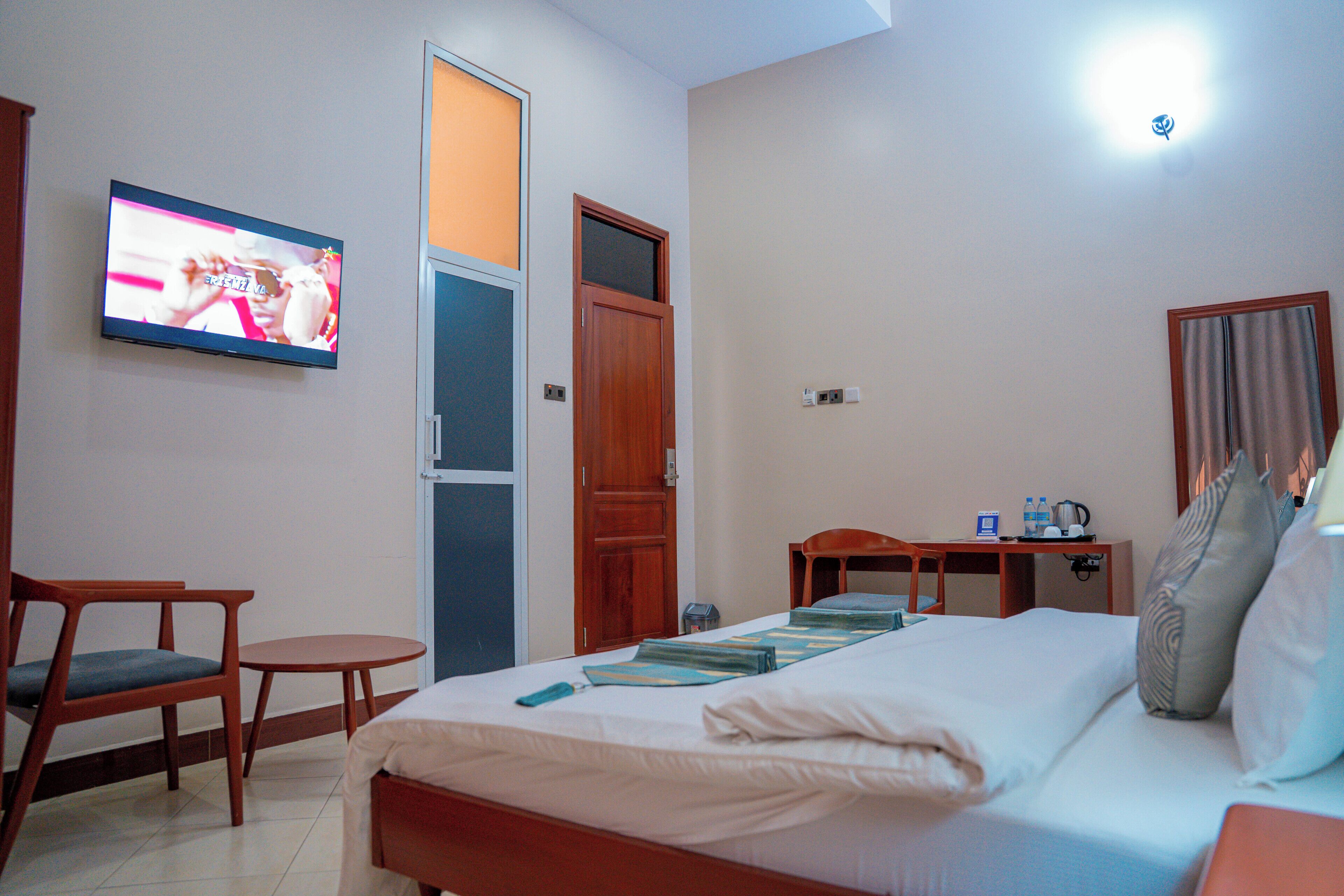 A hotel room with a bed, a television, a desk with a chair, and a small table.