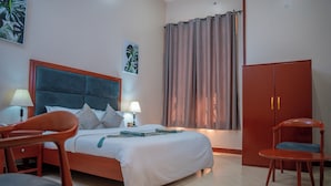 A bedroom with a bed, two chairs, a wardrobe, a nightstand, and a lamp. - Rostel Villa Hotel (Mbeya)