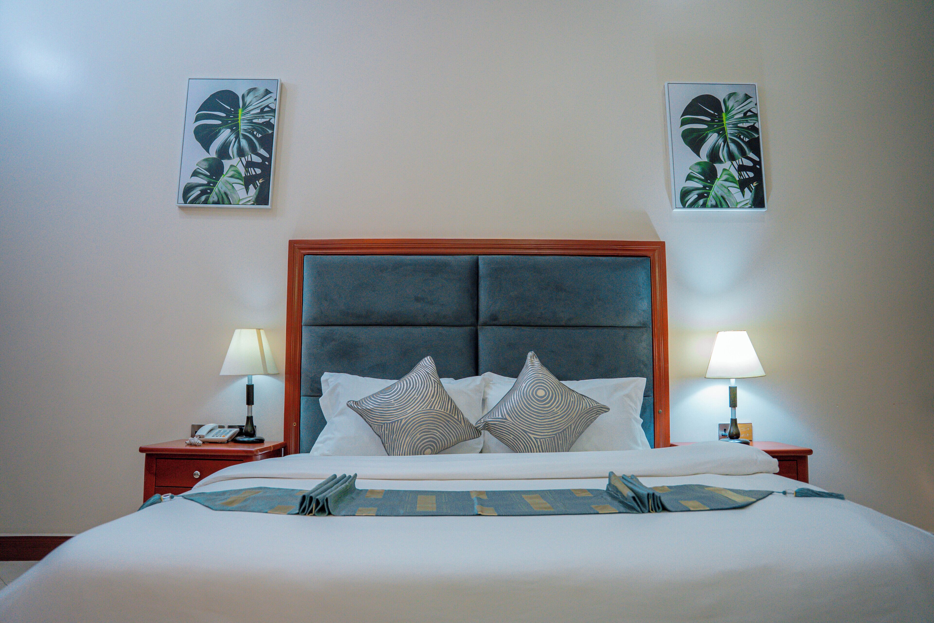 A hotel room with a bed, two bedside tables, two lamps, and two wall-mounted paintings.