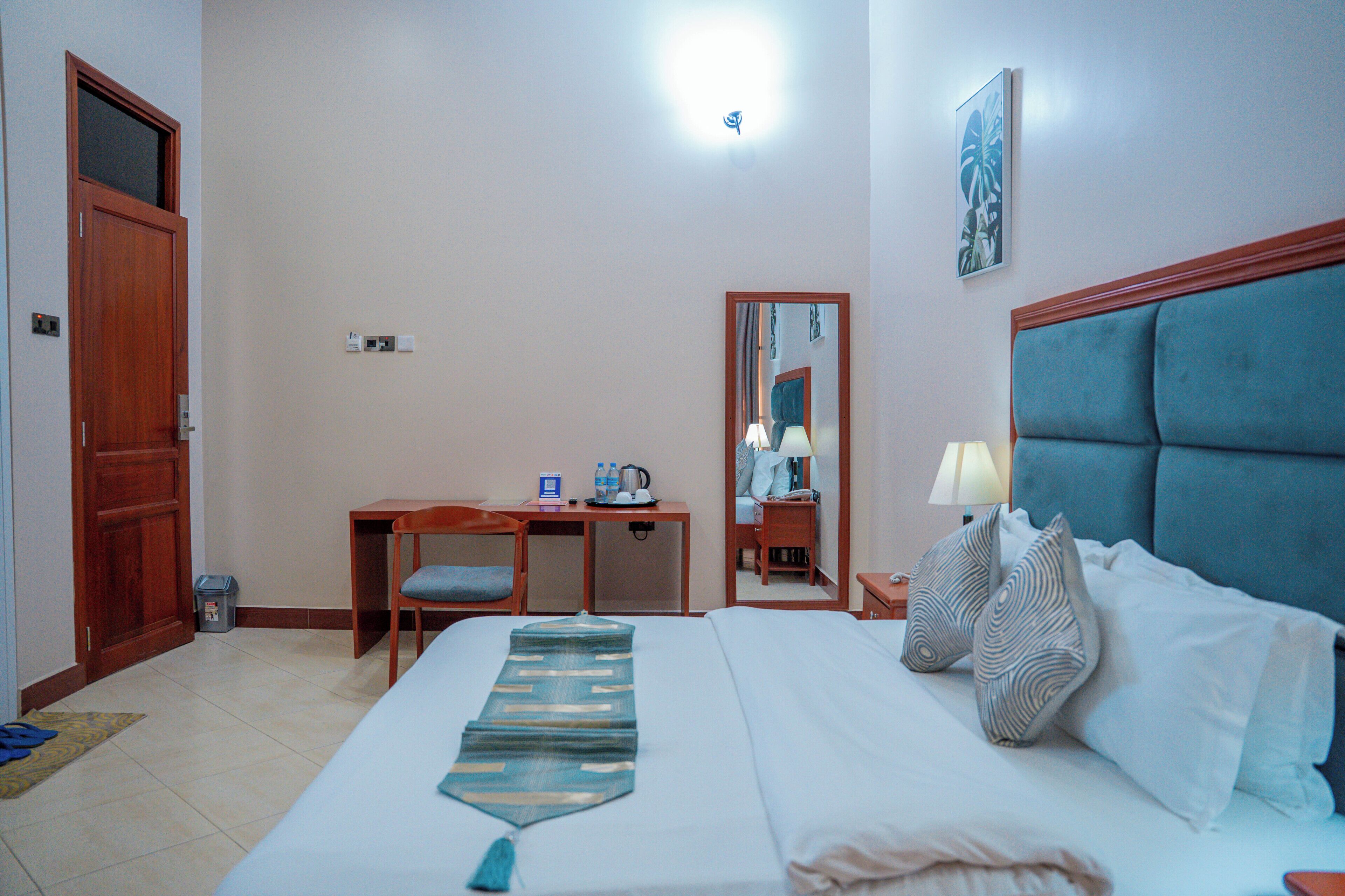 Una camera d'albergo con un letto, una scrivania, una sedia, uno specchio, una lampada e una porta.