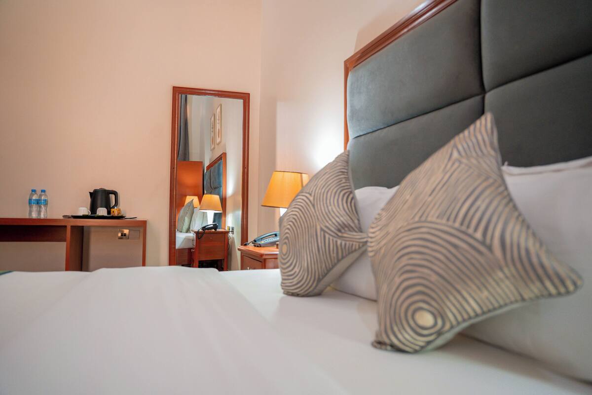 A hotel room with a bed, a desk with a coffee maker, a lamp, and a mirror.