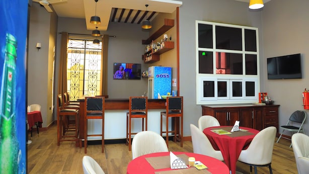 A dining area with wooden chairs and tables, a bar area with a TV, and a large window with a view. - Rostel Villa Hotel (Mbeya)