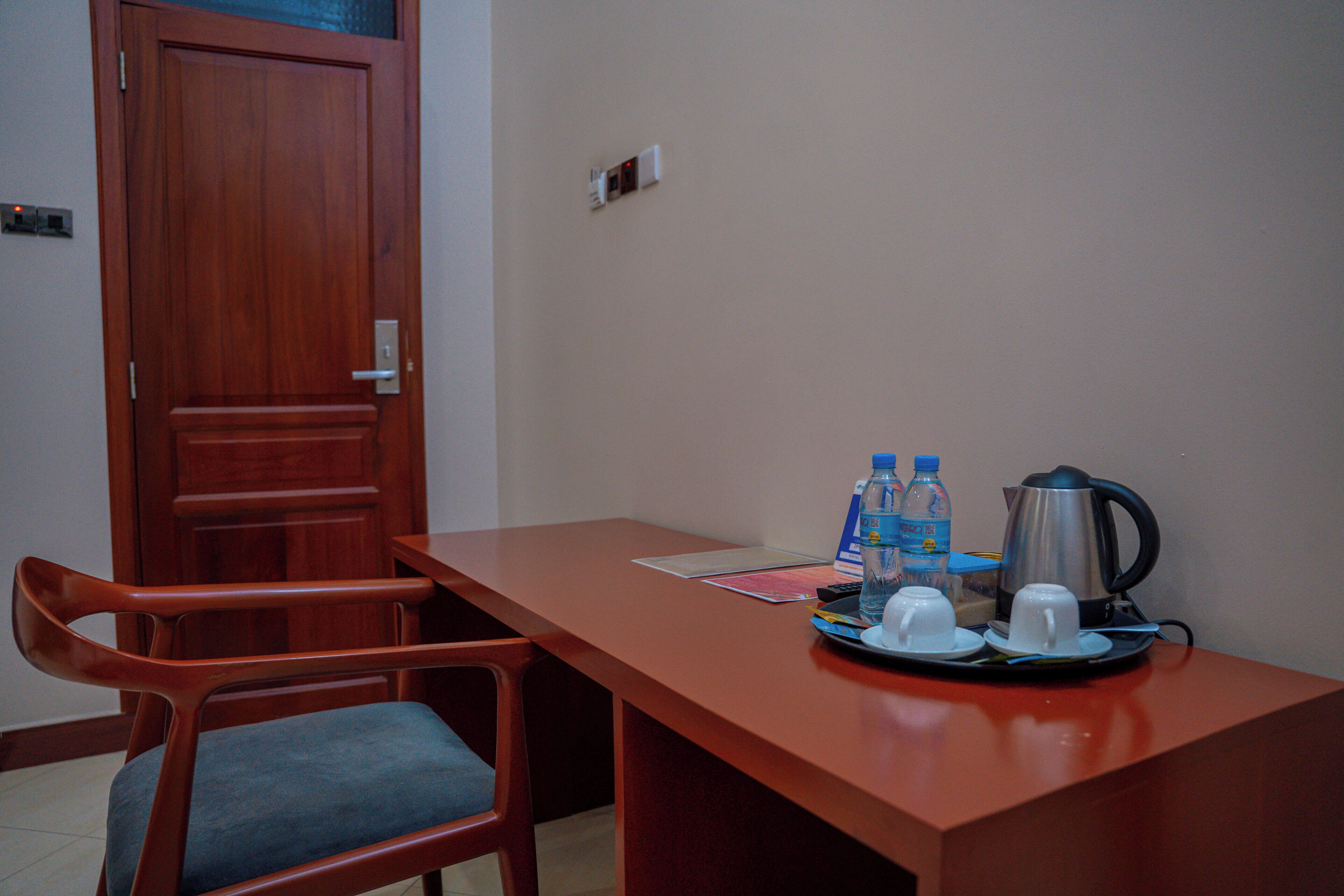 A hotel room with a wooden door, a desk with a kettle, cups, and water bottles.
