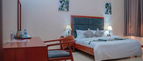 A hotel room with a bed, two bedside lamps, a desk with a chair, and two wall-mounted pictures.