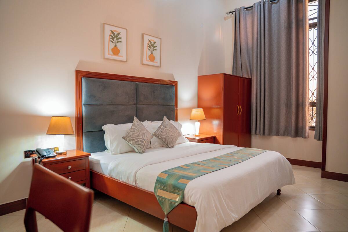 A hotel room with a bed, bedside tables, a wardrobe, and artwork on the wall.