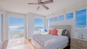 Een slaapkamer met een groot bed, een plafondventilator en uitzicht op het strand.