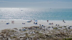 Een strand met mensen die zonnebaden en wandelen, en een boot in de verte.