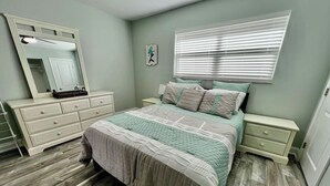 Un dormitorio con cama, mesitas de noche, cómoda, espejo y ventana con persianas.
