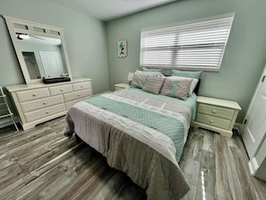 Un dormitorio con cama, mesitas de noche, cómoda, espejo y ventana con persianas.