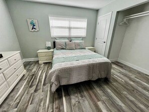 A bedroom with a bed, dresser, nightstands, and a window with blinds.