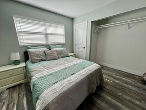 A bedroom with a bed, nightstand, lamp, window with blinds, and a door.