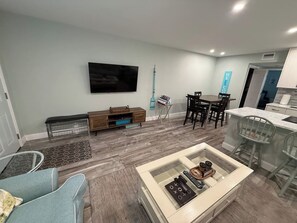 A modern living room with a flat-screen TV, a coffee table, and a dining area with chairs and a table.