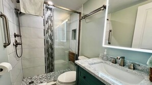 Un baño con cabina de ducha de vidrio, inodoro y lavamanos con encimera de mármol.
