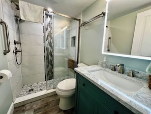 Un baño con cabina de ducha de vidrio, inodoro y lavamanos con encimera de mármol.