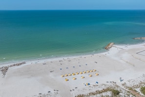 Vista aérea de una playa con hileras de sombrillas amarillas y una orilla arenosa.