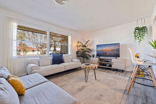 Ein modernes Wohnzimmer mit Sofa, Fernseher, Couchtisch und einer Pflanze.