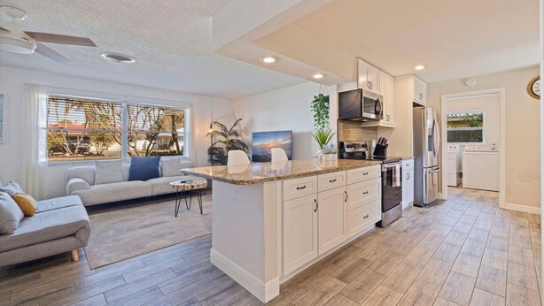 A modern kitchen with white cabinetry, a granite countertop, and stainless steel appliances. - Sunny Home & Yard, Minutes to Beach (Seminole)