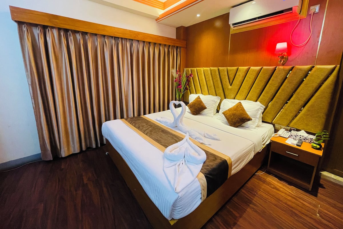 Ein Hotelzimmer mit einem großen Bett, einem Holzkopfende, einer Klimaanlage, einem Nachttisch mit Lampe und einem Fenster mit Vorhängen.
