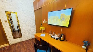 A hotel room with a wooden desk, a television mounted on the wall, a mirror, and a vase with yellow flowers. - Hotel Rosewood Uttara (Dhaka)