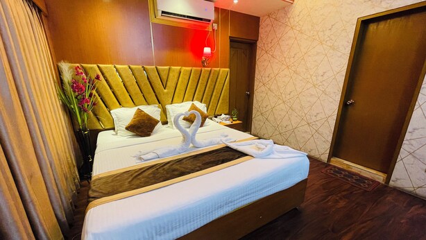 A hotel room with a bed, a wooden headboard, a wall-mounted air conditioner, and a door. - Hotel Rosewood Uttara (Dhaka)