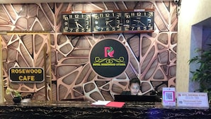 Un comptoir d’accueil avec une horloge, une enseigne indiquant le café Rosewood et le logo de l’hôtel Rosewood Uttara.