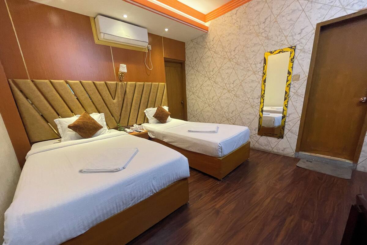 Ein Hotelzimmer mit zwei Betten, einem Holzkopfende, einer Wand mit Marmoroptik, einer Klimaanlage und einem Spiegel mit Zierrahmen.