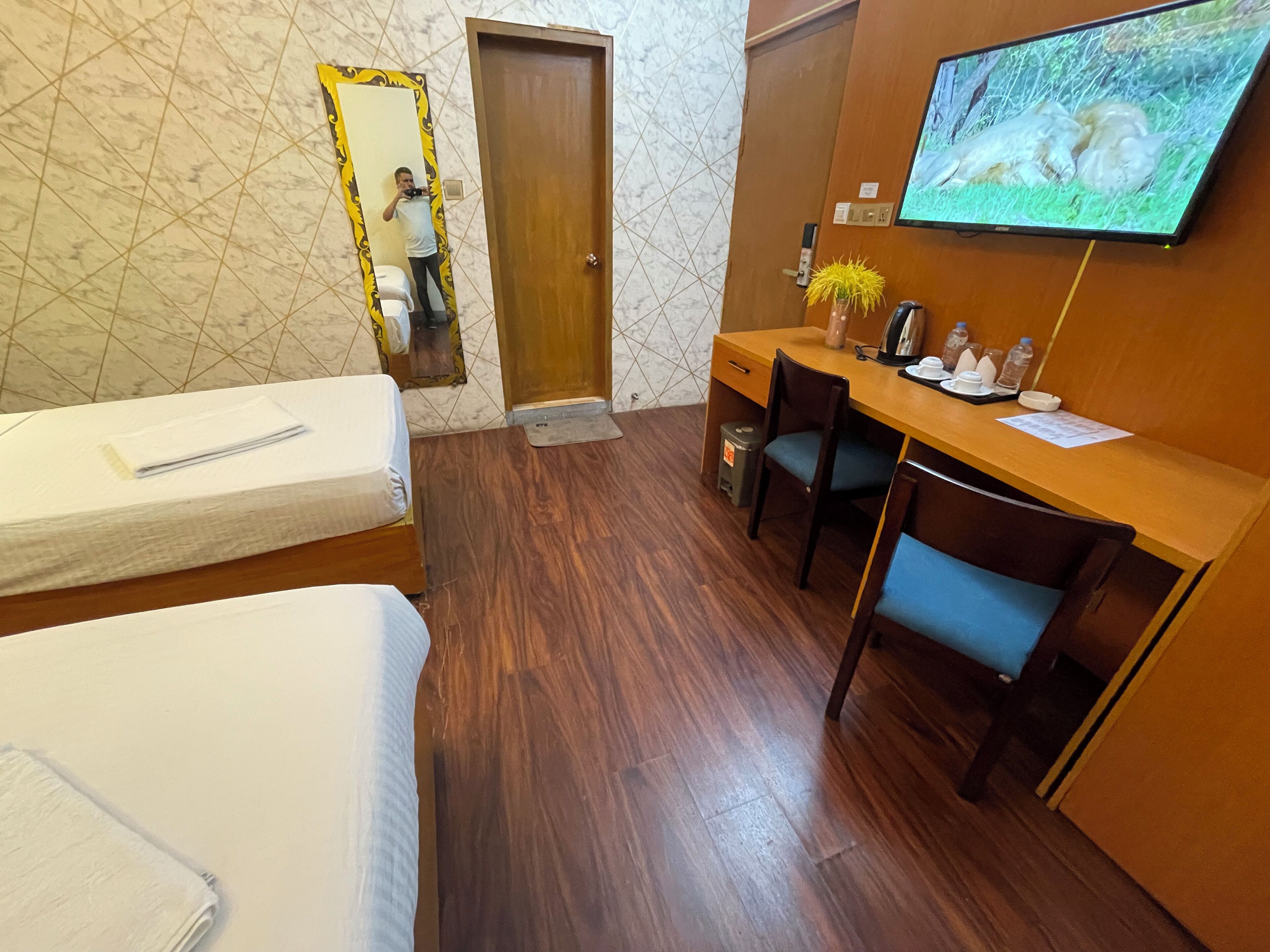 A hotel room with a bed, a desk, a chair, a television, and a mirror.