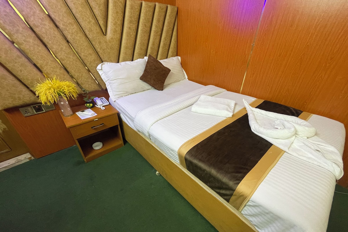 Ein Hotelzimmer mit einem Bett, einem Nachttisch mit Telefon und einer Vase sowie einem grünen Teppich.