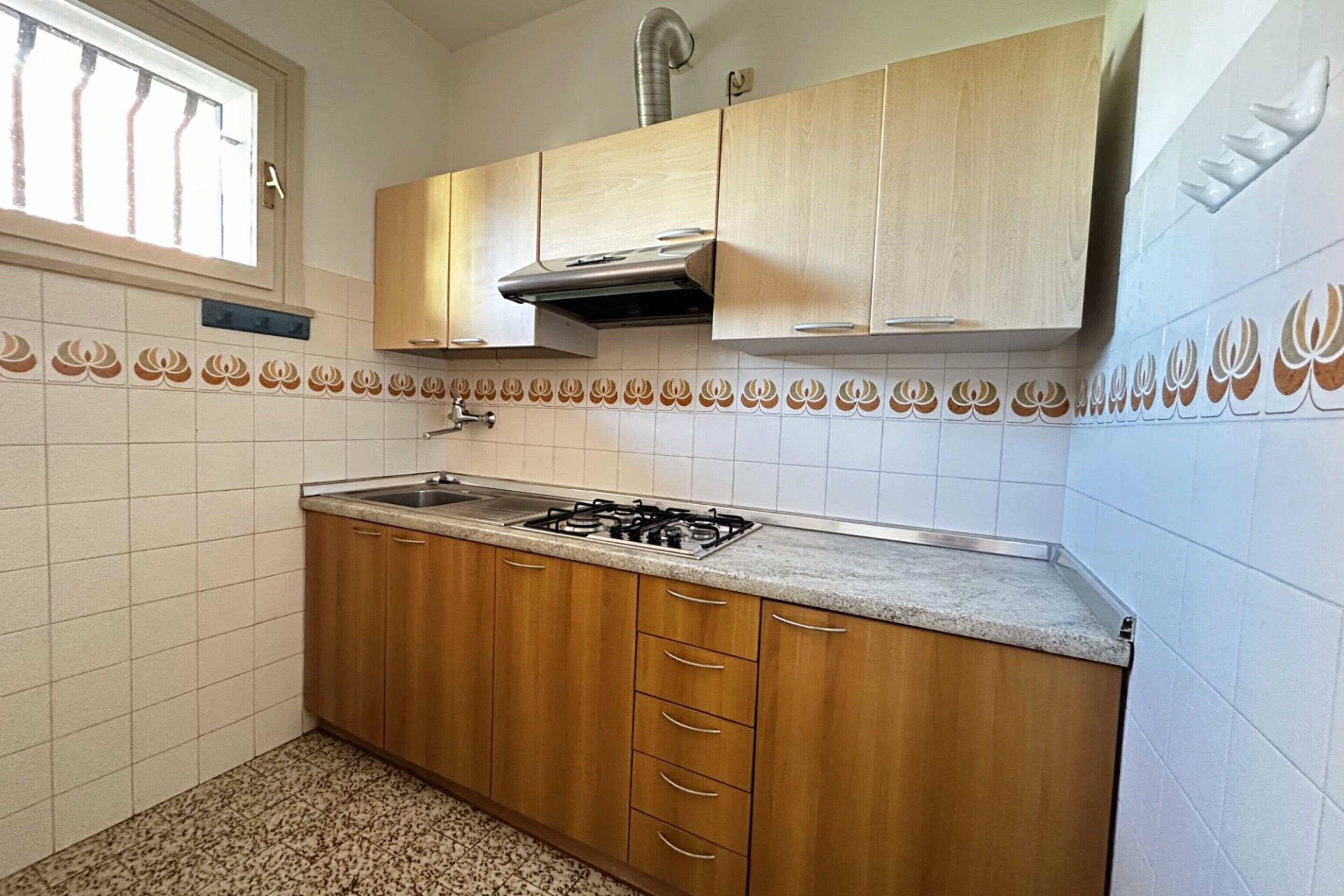 A kitchen with wooden cabinets, a gas stove, and a window with blinds.