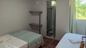 A small, well-lit room with two beds, a shower, and a window with curtains.