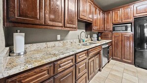 A kitchen with wooden cabinets, granite countertops, a stainless steel refrigerator, and a microwave. - Private Fort Worth Getaway Near Botanic Garden! (Fort Worth)