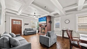 A spacious living room with hardwood flooring, a fireplace, a ceiling fan, and a large window. - Private Fort Worth Getaway Near Botanic Garden! (Fort Worth)