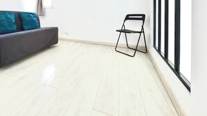 A minimalist room with a dark grey sofa, teal cushions, a black folding chair, and a white shelf.