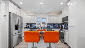 A modern kitchen with white cabinets, stainless steel appliances, and a central island with orange bar stools. - Unique Shipping Container Stay - Walk to Branson Landing! (Branson)