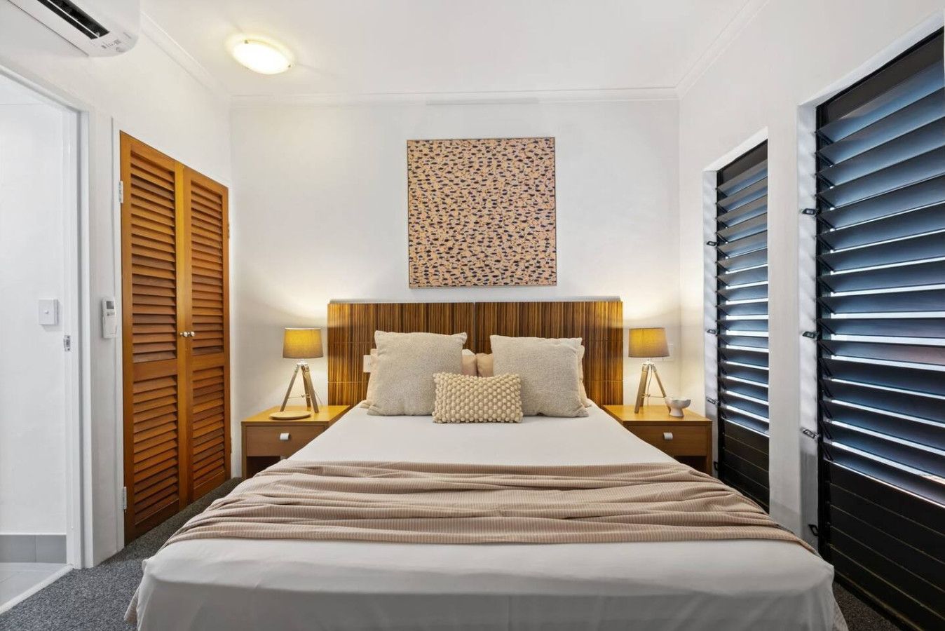 A bedroom with a large bed, wooden headboard, two bedside tables with lamps, and a wall-mounted artwork.