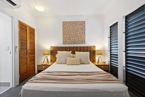 A bedroom with a large bed, wooden headboard, two bedside tables with lamps, and a wall-mounted artwork.