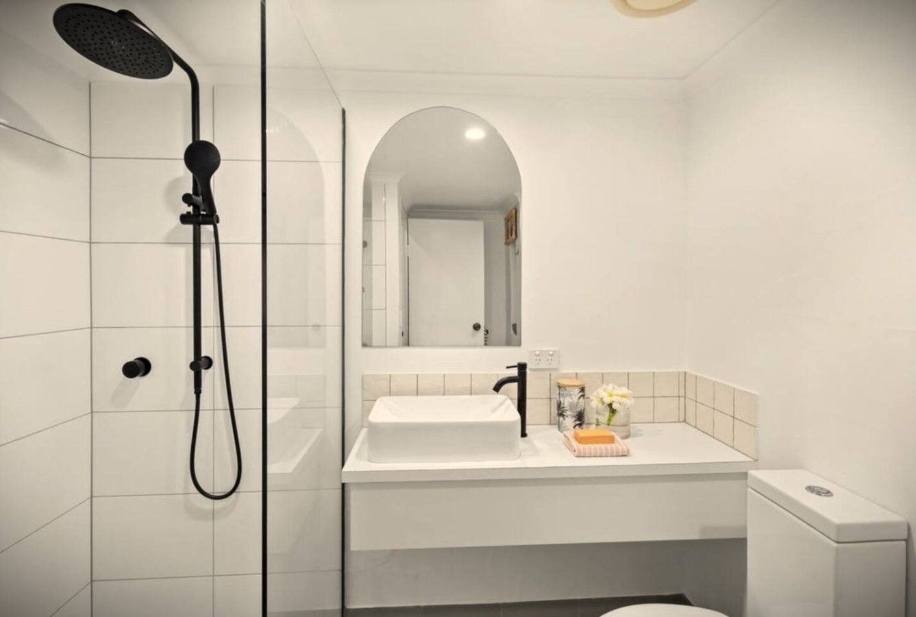 A modern bathroom with a white sink, a mirror, and a shower.