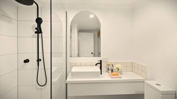 A modern bathroom with a white sink, a mirror, and a shower.