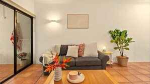 Ein Wohnzimmer mit grauem Sofa, Couchtisch aus Holz, Blumen in einer Vase und einer Topfpflanze, sowie einer Glasschiebetür.
