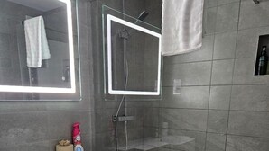 A modern bathroom with a glass-enclosed shower, a white toilet, a sink with a mirror, and a towel hanging on the wall.