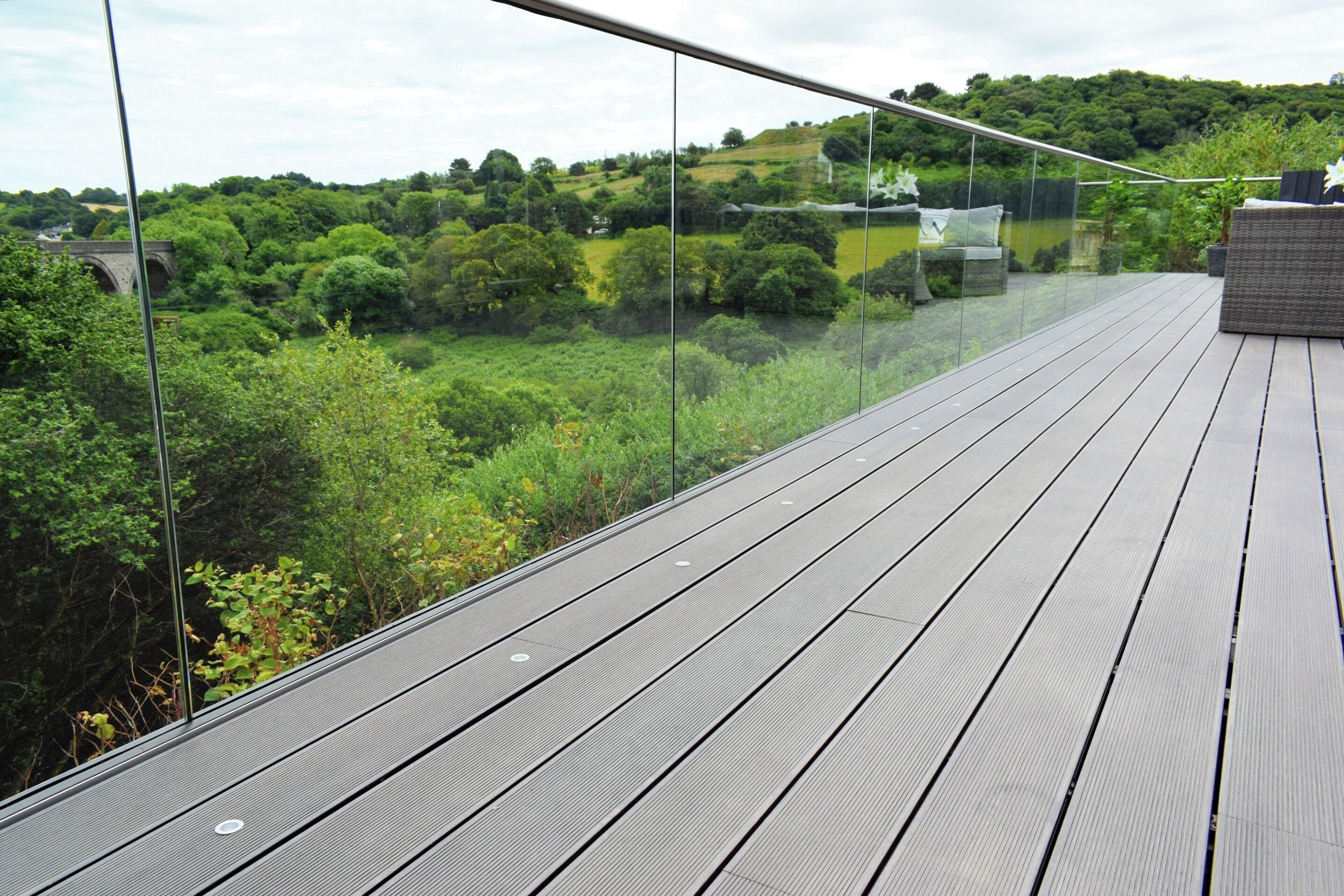 Una terraza con barandilla de cristal que da a un paisaje verde exuberante.