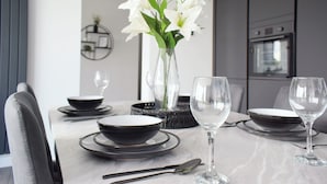 A modern dining table set with plates, bowls, and cutlery, accompanied by a vase of white flowers.