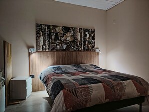 A bedroom with a bed, a headboard, a wall-mounted artwork, a bedside table, and a nightstand.