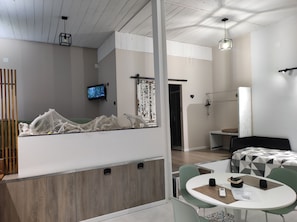 A modern hotel room with a bed, a dining table, a TV, and a view of the outside.
